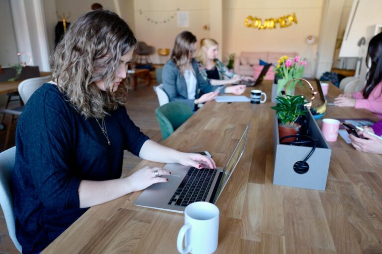 Group of women working in a modern coworking space with laptops and coffee.